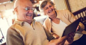 Happy senior couple sitting at home and using touchpad together.