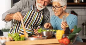 Smiling, senior couple preparing a meal of fresh vegetables in a home kitchen.